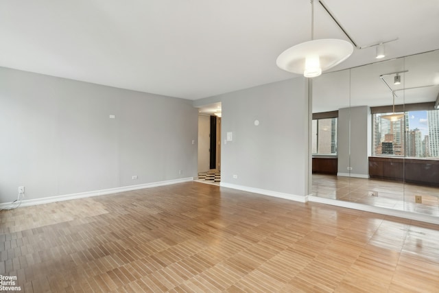 unfurnished room featuring rail lighting and baseboards