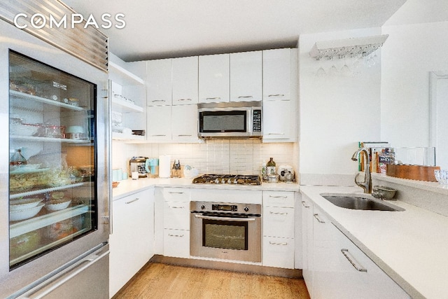 kitchen featuring appliances with stainless steel finishes, light wood-type flooring, white cabinets, decorative backsplash, and sink