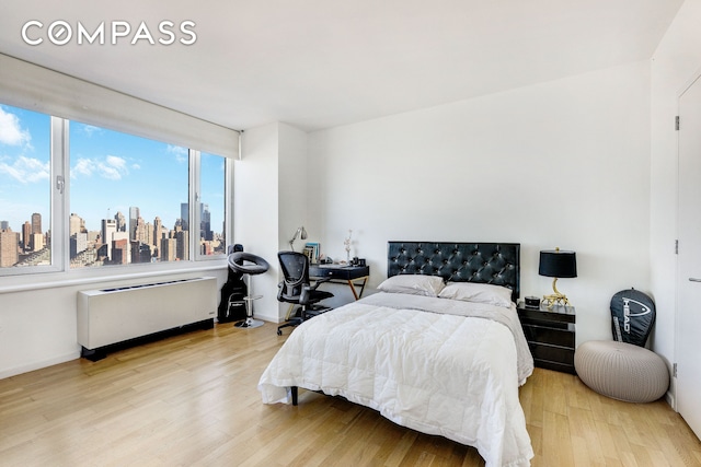 bedroom featuring a city view, radiator heating unit, wood finished floors, and baseboards