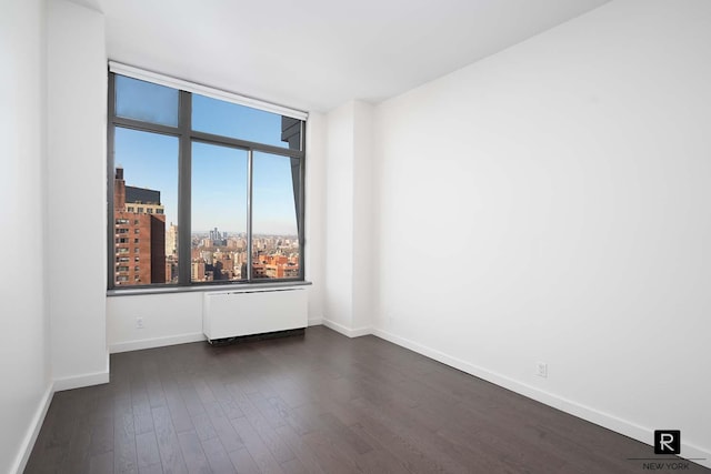 spare room featuring baseboards, a view of city, and dark wood finished floors