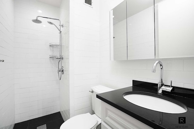 bathroom with a tile shower, backsplash, visible vents, toilet, and tile walls