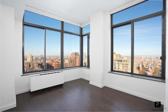 unfurnished room featuring dark wood-style floors, baseboards, a city view, and radiator heating unit