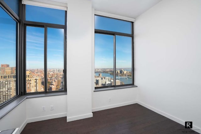 unfurnished room featuring a view of city, dark wood-style flooring, a water view, and baseboards