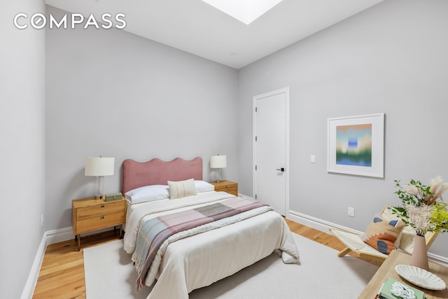 bedroom featuring a skylight, light wood-style flooring, and baseboards