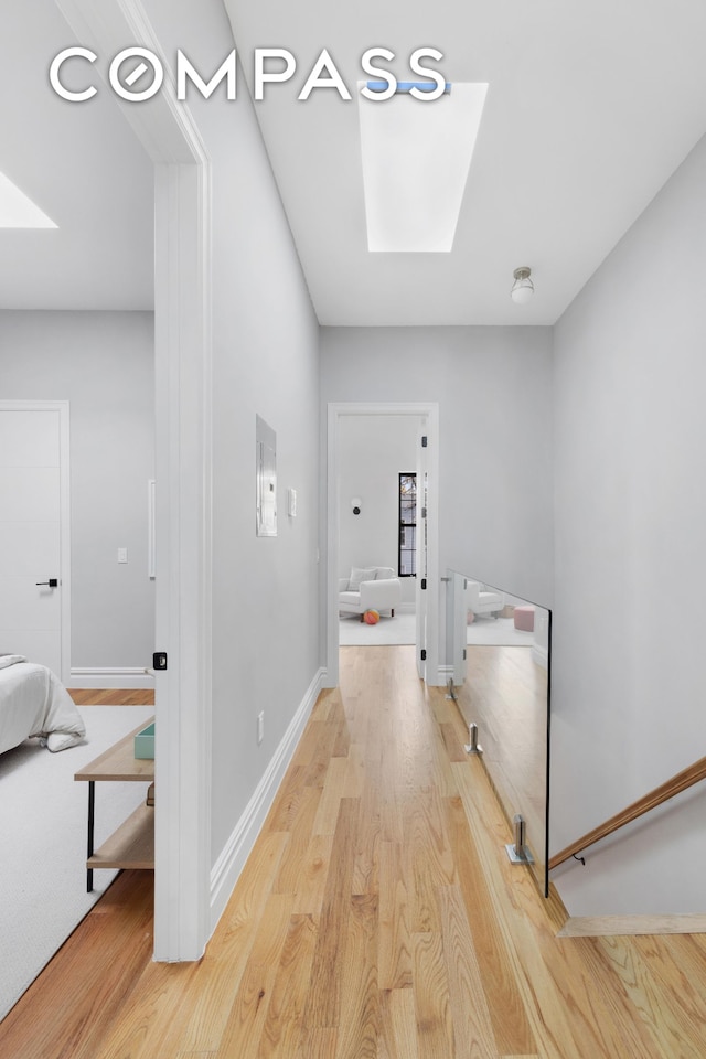 hallway with baseboards, a skylight, and light wood finished floors