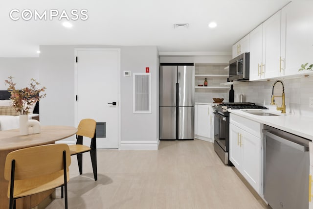 kitchen with a sink, light countertops, white cabinets, appliances with stainless steel finishes, and backsplash