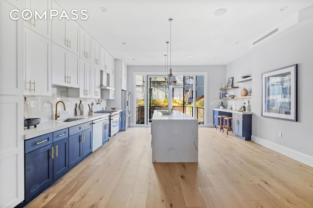 kitchen with light wood finished floors, white appliances, blue cabinets, and a sink