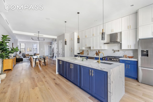 kitchen with blue cabinetry, light wood-type flooring, wall chimney range hood, and stainless steel fridge with ice dispenser