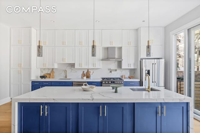 kitchen featuring backsplash, blue cabinetry, wall chimney range hood, premium appliances, and a sink