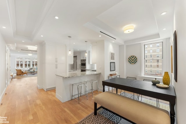 kitchen featuring white cabinetry, light hardwood / wood-style floors, kitchen peninsula, pendant lighting, and light stone counters