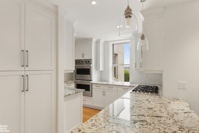 kitchen featuring decorative light fixtures, white cabinetry, light hardwood / wood-style flooring, light stone countertops, and appliances with stainless steel finishes