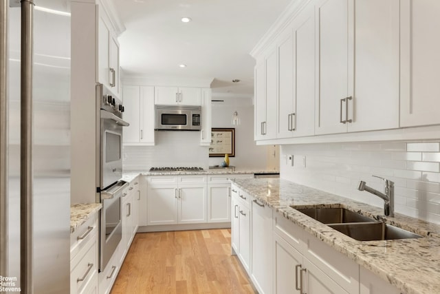 kitchen with appliances with stainless steel finishes, white cabinetry, light hardwood / wood-style floors, sink, and light stone counters