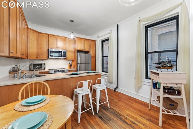 kitchen with decorative light fixtures, dark hardwood / wood-style flooring, kitchen peninsula, stainless steel appliances, and crown molding