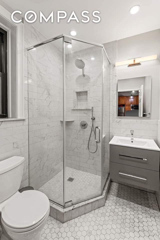 full bathroom with tile walls, toilet, vanity, a shower stall, and tile patterned floors