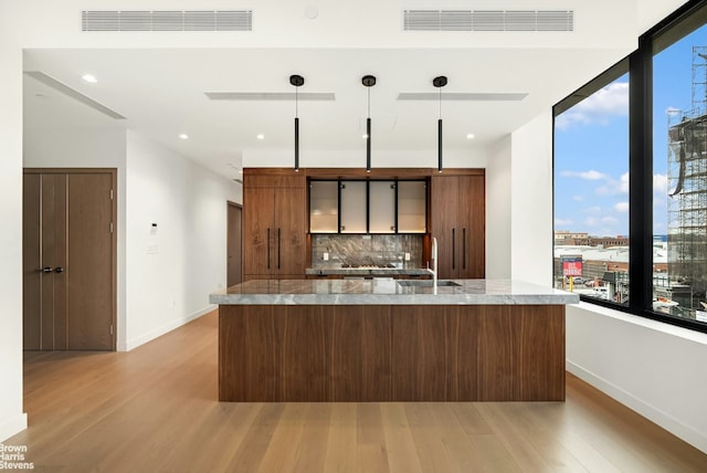 kitchen featuring hanging light fixtures, sink, light wood-type flooring, and decorative backsplash