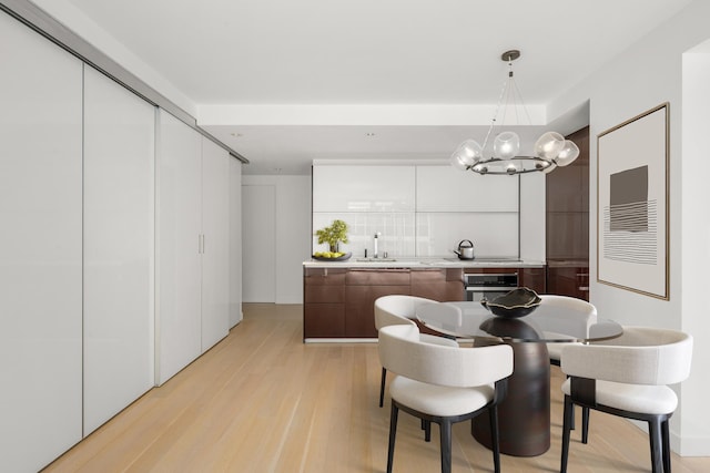 kitchen with light wood finished floors, light countertops, stainless steel oven, a sink, and modern cabinets