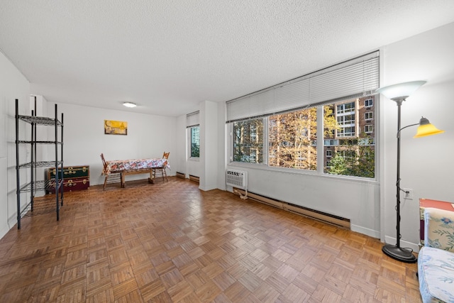 sitting room with a textured ceiling, a baseboard radiator, a healthy amount of sunlight, and parquet flooring