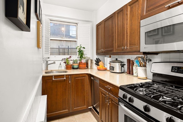 kitchen featuring a sink, light countertops, appliances with stainless steel finishes, brown cabinets, and backsplash