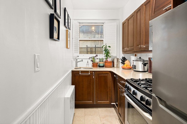 kitchen featuring a wainscoted wall, a sink, stainless steel appliances, light tile patterned flooring, and light countertops