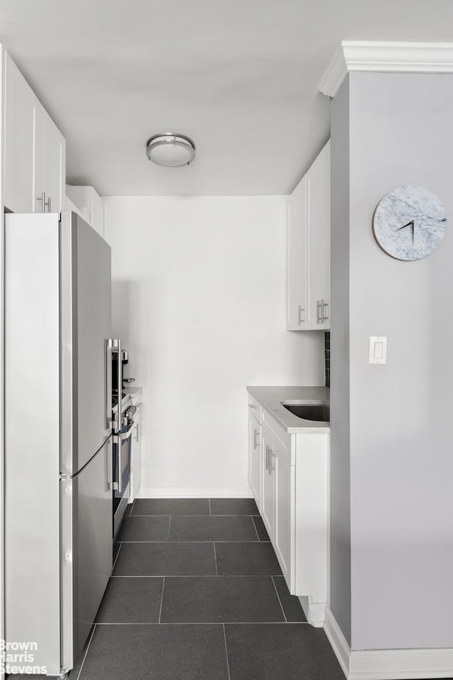 kitchen with baseboards, white cabinetry, freestanding refrigerator, stove, and dark tile patterned flooring