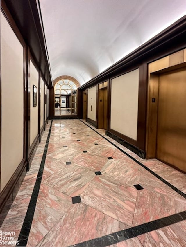 hallway featuring lofted ceiling, marble finish floor, elevator, and baseboards