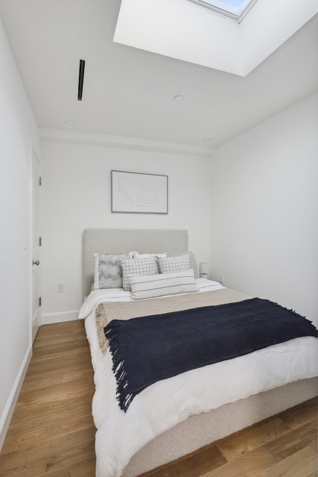 bedroom with a skylight, baseboards, and wood finished floors