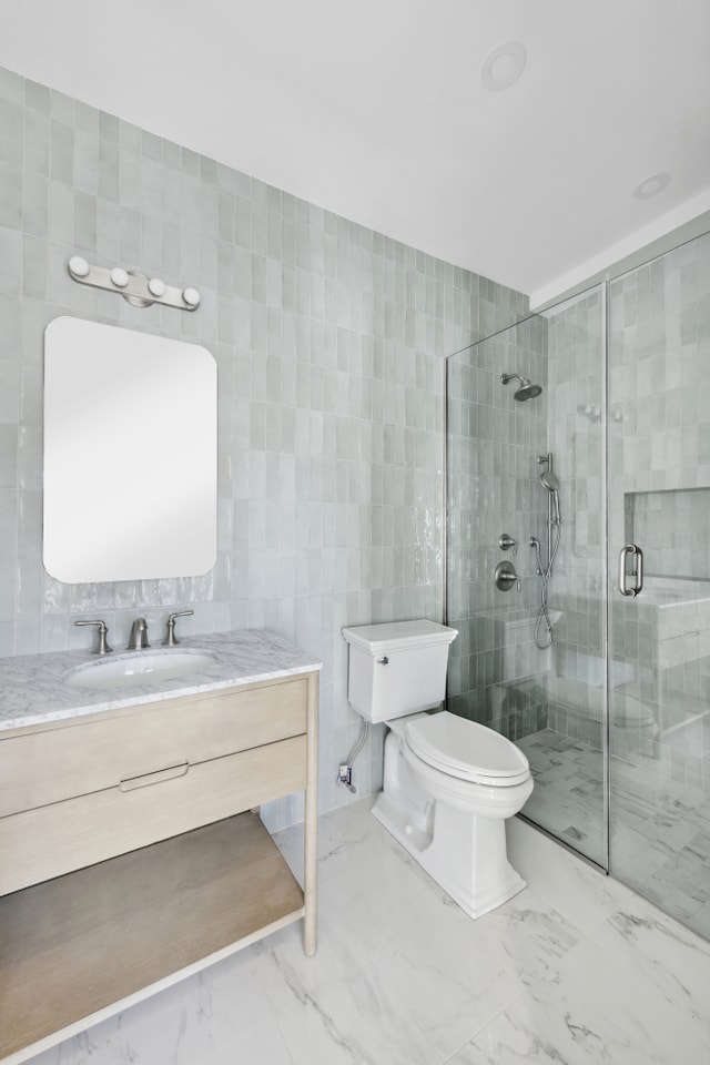 bathroom featuring toilet, vanity, tile walls, marble finish floor, and a stall shower