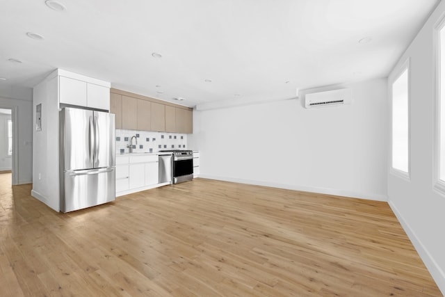 kitchen with a wall unit AC, light wood finished floors, stainless steel appliances, decorative backsplash, and a sink