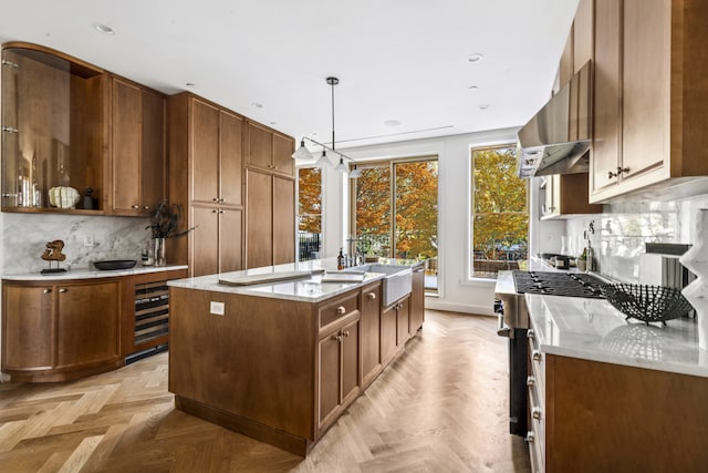 kitchen with wine cooler, decorative backsplash, an island with sink, stainless steel gas range oven, and extractor fan