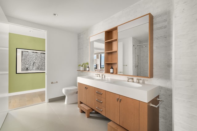 bathroom with double vanity, tiled shower, toilet, and a sink