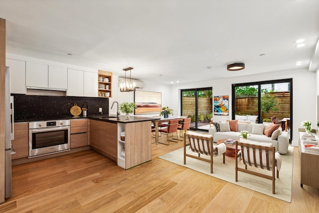 kitchen with dark countertops, a peninsula, open shelves, stainless steel oven, and light wood-type flooring