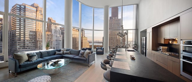 living room with a towering ceiling, wood finished floors, a city view, floor to ceiling windows, and a notable chandelier