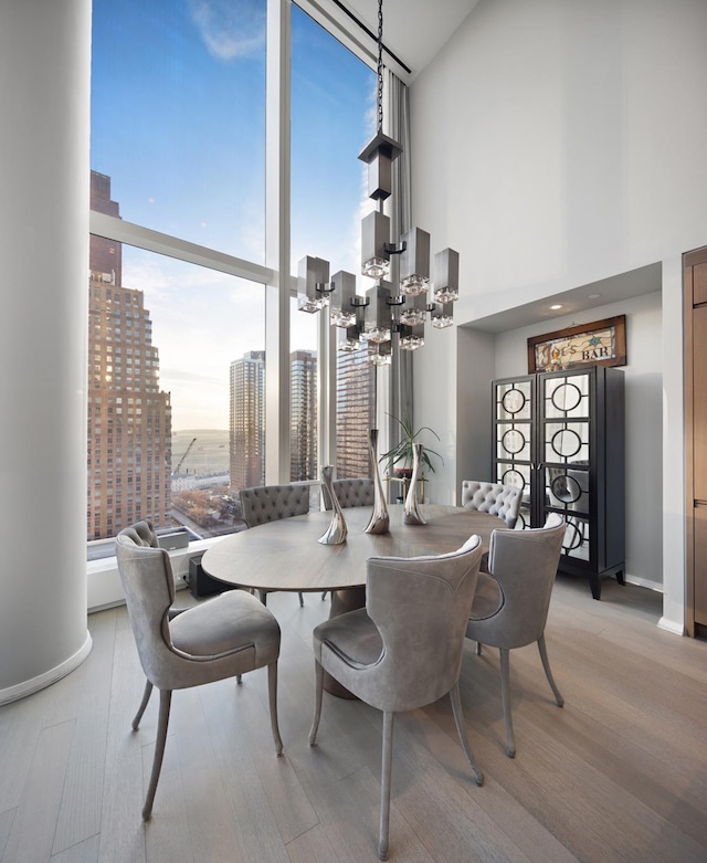 dining space with a chandelier, light wood-style floors, baseboards, a city view, and a wall of windows