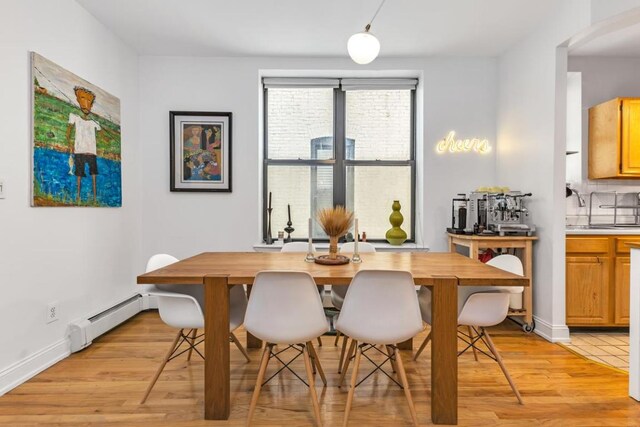 dining area with a baseboard radiator, light wood-style flooring, and baseboards