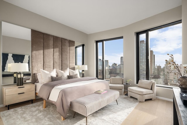 bedroom featuring a city view, light wood-style floors, and baseboards