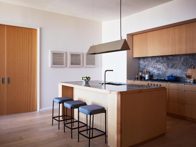 kitchen with light wood-type flooring, tasteful backsplash, modern cabinets, and a breakfast bar area