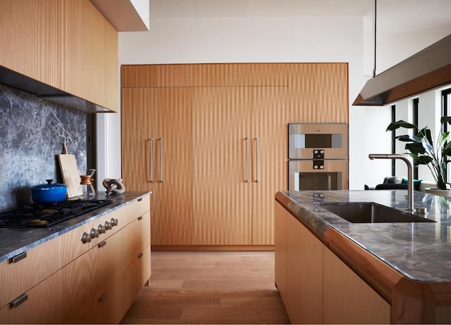 kitchen with a sink, gas cooktop, stainless steel double oven, light wood-style floors, and decorative backsplash