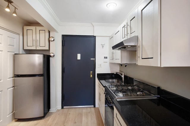 kitchen featuring freestanding refrigerator, crown molding, under cabinet range hood, a sink, and gas stove