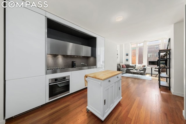 kitchen with white cabinets, tasteful backsplash, dark hardwood / wood-style floors, oven, and butcher block countertops