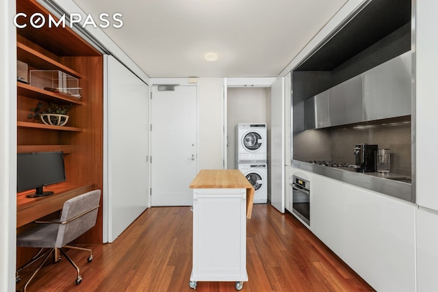 kitchen with oven, butcher block countertops, dark wood-type flooring, and stacked washing maching and dryer