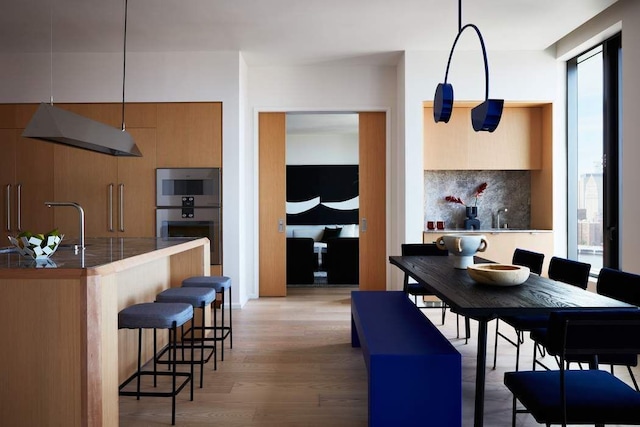 kitchen with sink, a breakfast bar area, tasteful backsplash, pendant lighting, and light hardwood / wood-style floors