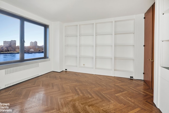 spare room featuring radiator heating unit, a water view, and a city view