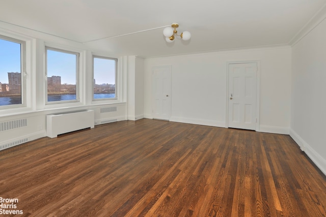 empty room with a notable chandelier, radiator, a water view, dark wood-type flooring, and baseboards