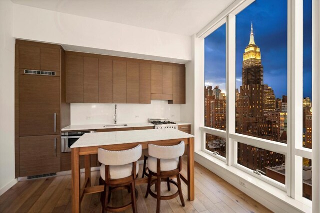 kitchen with oven, light hardwood / wood-style floors, a kitchen bar, sink, and expansive windows