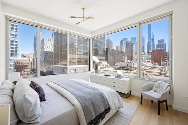 bedroom with a skyline view, a chandelier, wood finished floors, and baseboards