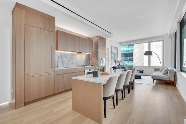 kitchen featuring sink, light hardwood / wood-style flooring, a breakfast bar, backsplash, and a kitchen island