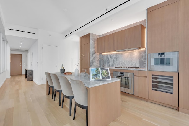 kitchen featuring decorative backsplash, stainless steel appliances, light hardwood / wood-style floors, and a kitchen bar