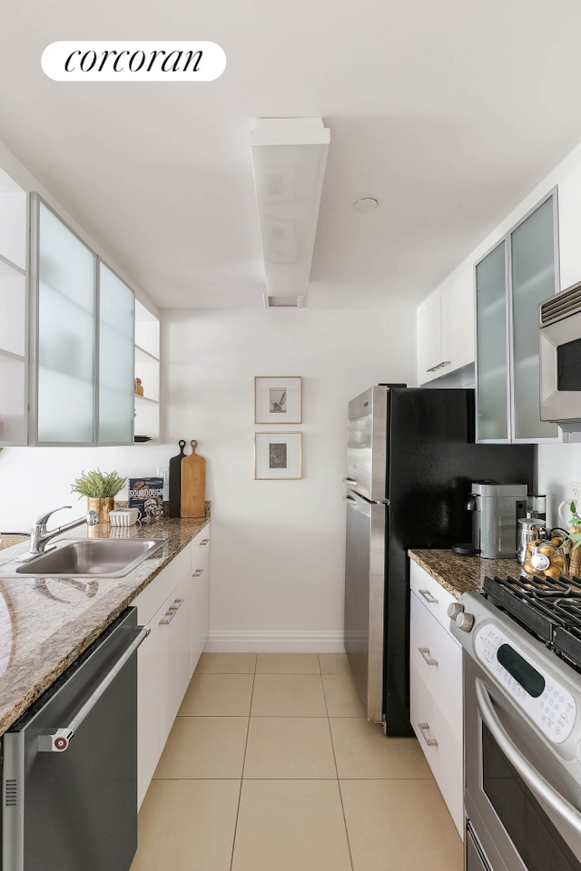 kitchen with stainless steel appliances, a sink, white cabinetry, and glass insert cabinets