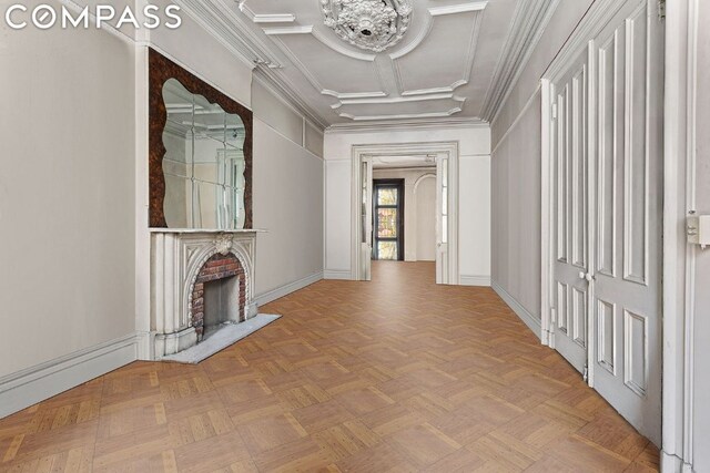 unfurnished living room featuring a brick fireplace, light parquet flooring, ornamental molding, and coffered ceiling