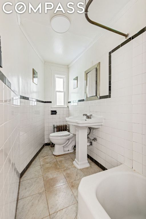 bathroom featuring toilet, crown molding, tile walls, and a washtub